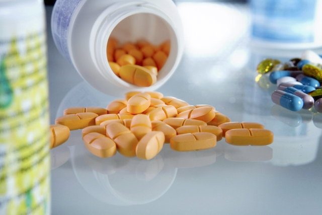 Suplementos de L-carnitina em cápsulas e pó sobre uma mesa com alimentos ricos em aminoácidos.